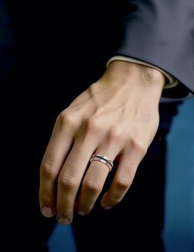 Male hand wearing a modern platinum wedding band with black diamonds, featuring an elegant ribbon-like design.